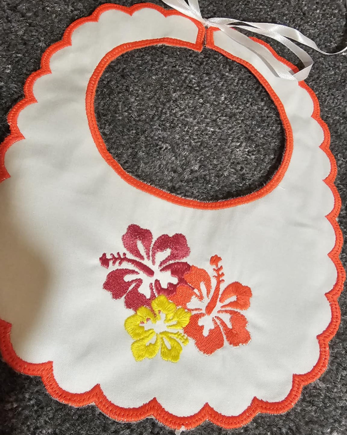 Embroidered bib with floral design on a dark surface